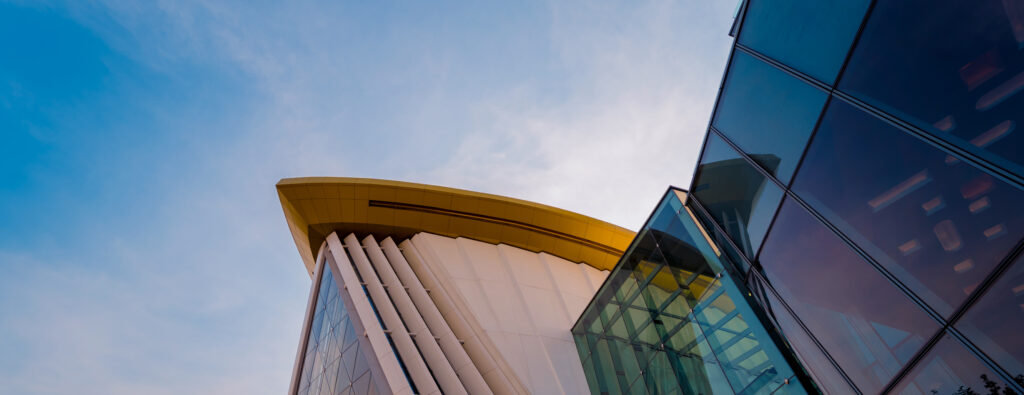 Modern architectural design featuring sleek glass and angular structures under a bright blue sky.