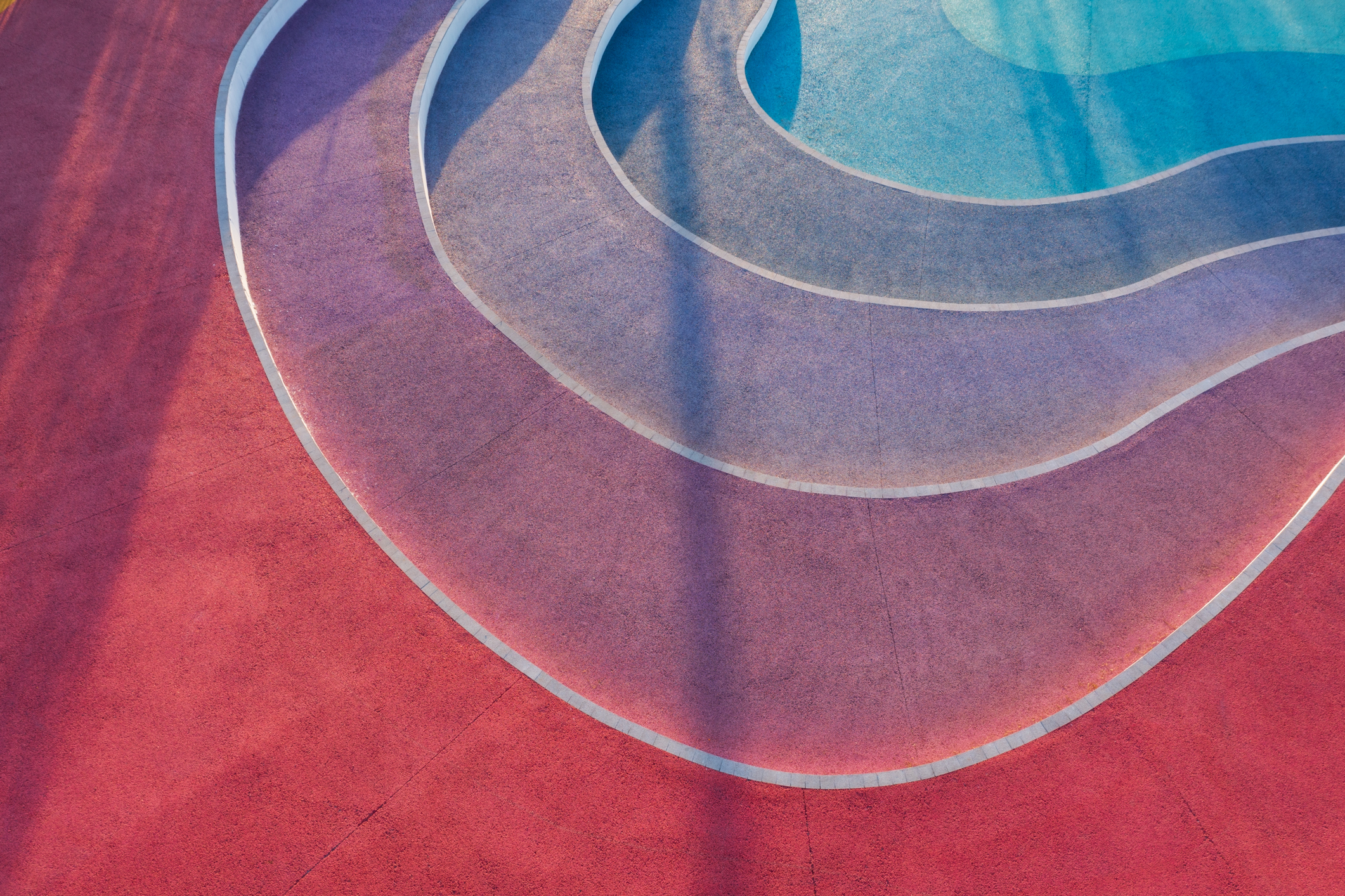 Aerial view of curved, colorful patterns on a stepped surface, featuring shades of red, purple, and blue intertwined with white lines.