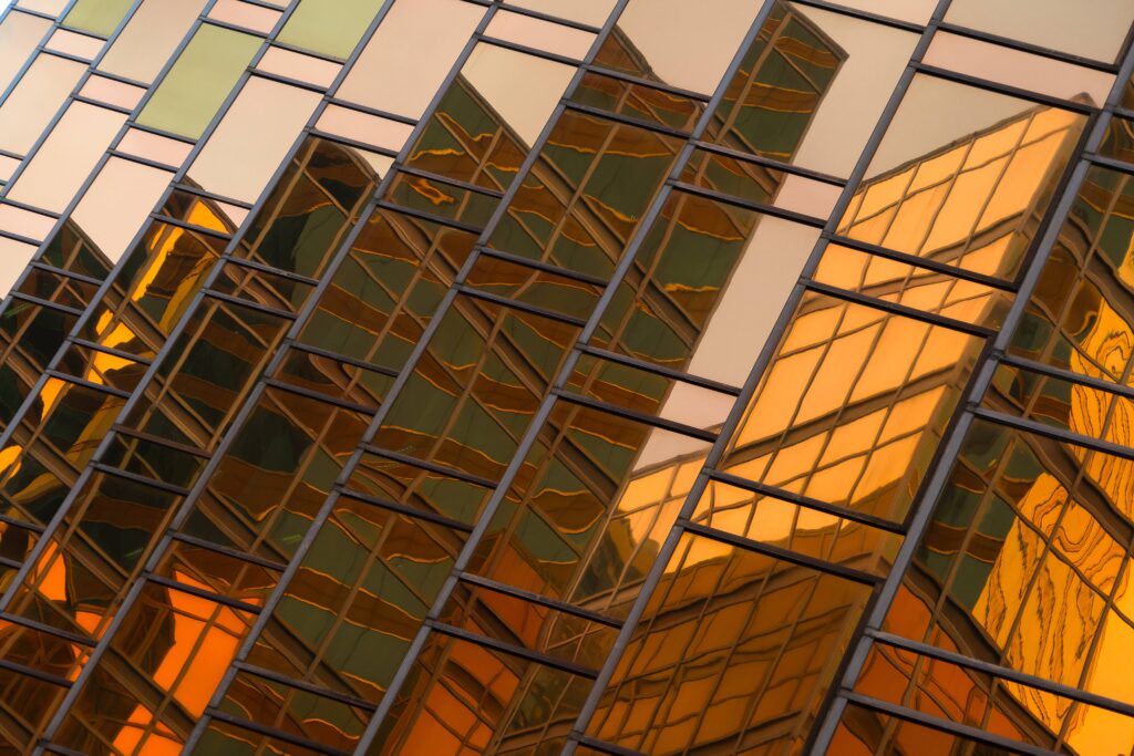 Abstract reflections of buildings shimmer in golden and green hues across the glass facade, creating a striking geometric pattern.
