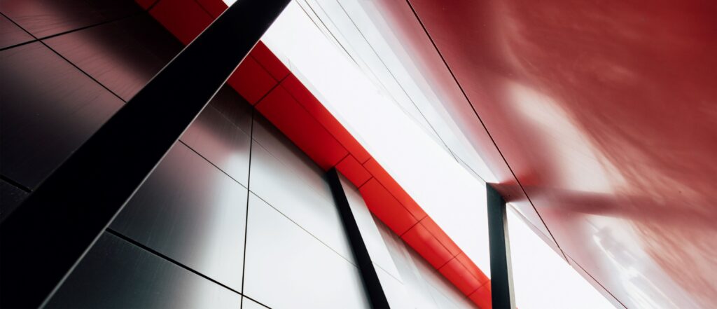 Abstract view of a modern building's sharp lines, featuring sleek metallic surfaces and a vibrant red accent.