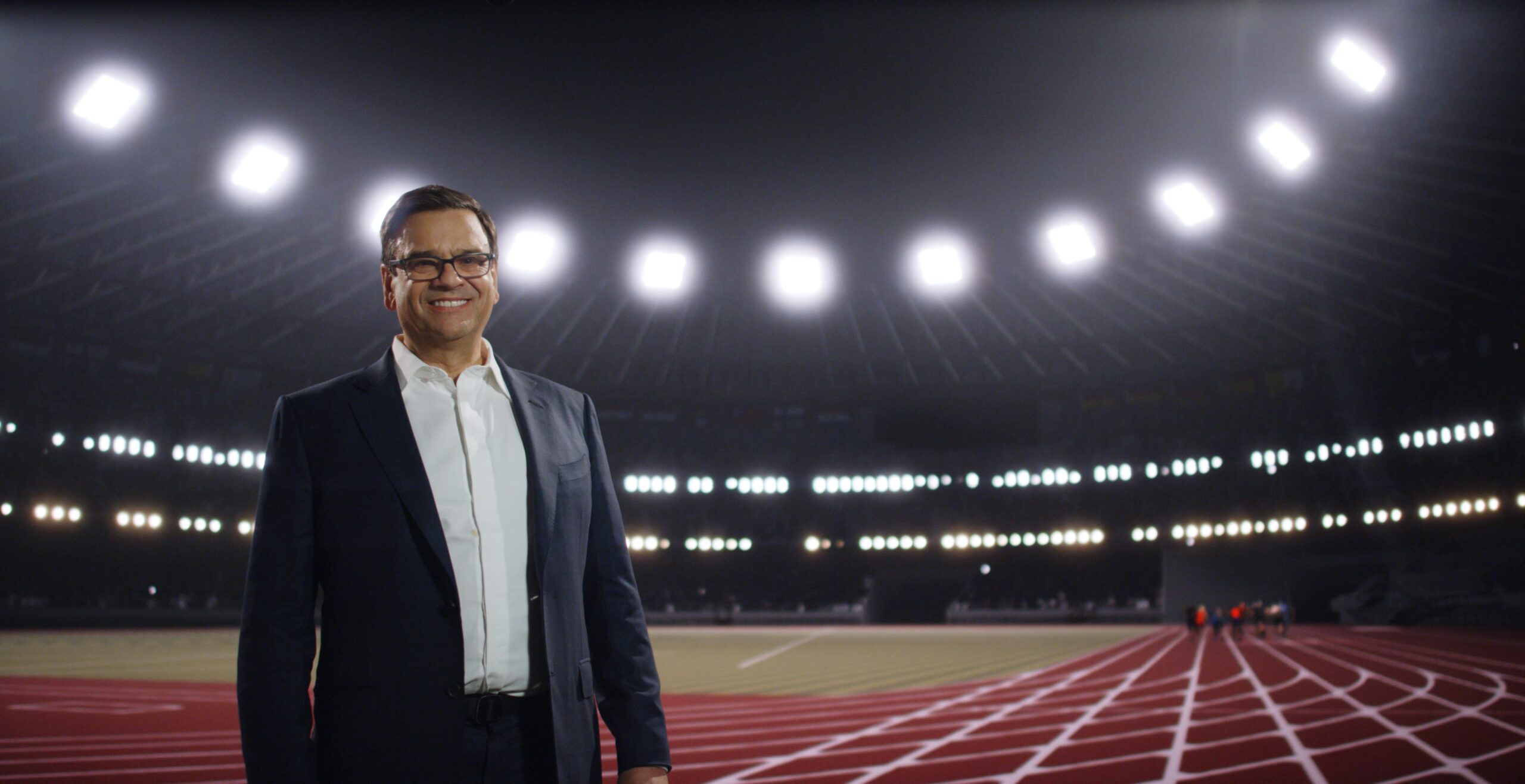 Jeremy Collers smiles whilst standing on a running track in an athletics stadium.